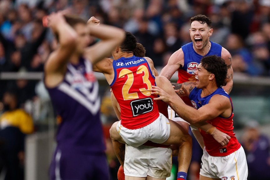Brisbane players celebrate wildly as a Fremantle player holds his head in his hands