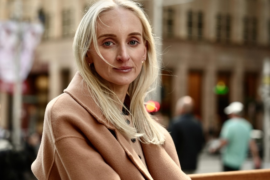 A close-up photo of Samantha Bouffler, wearing a tan coat, in a busy CBD setting
