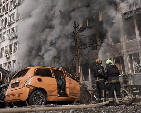 Firefighters extinguishing a fire at an office building with an orange car in foreground.