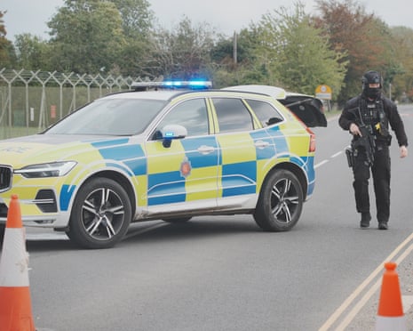 An armed police officer alongside a police car