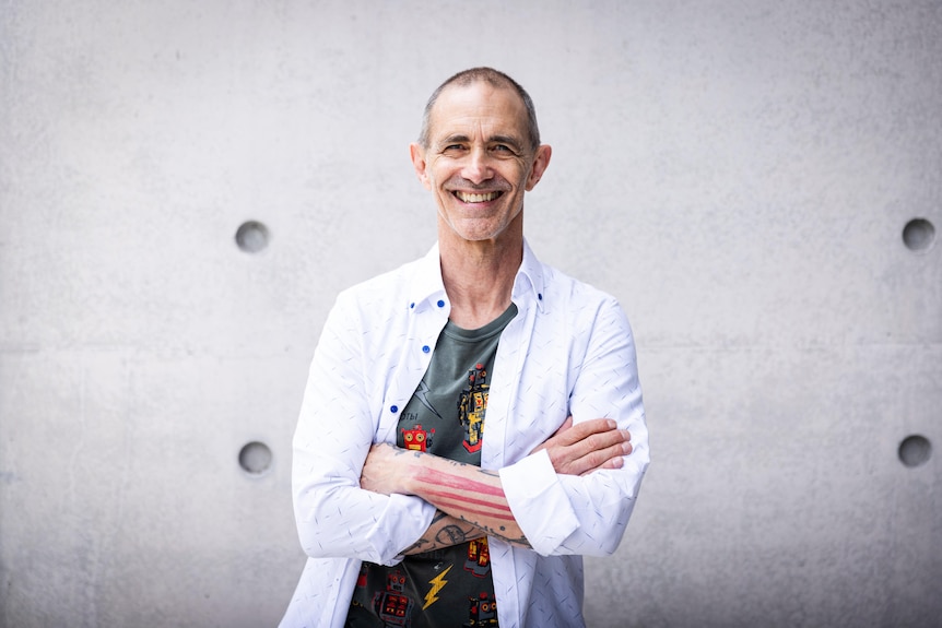 Andy Griffiths smiles with his tattooed arms crossed
