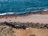 An aerial view of caravan and vehicle with waves and ocean beyond