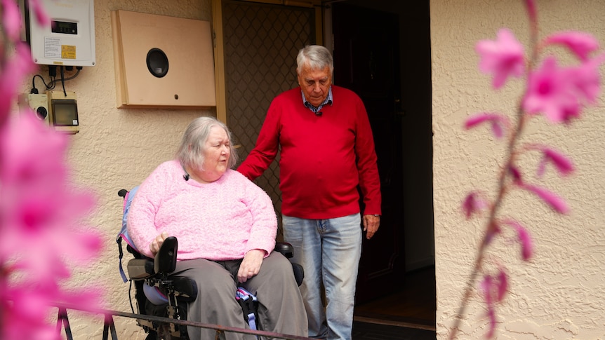 a woman in a wheelchair goes down a ramp. a man is standing next to her.